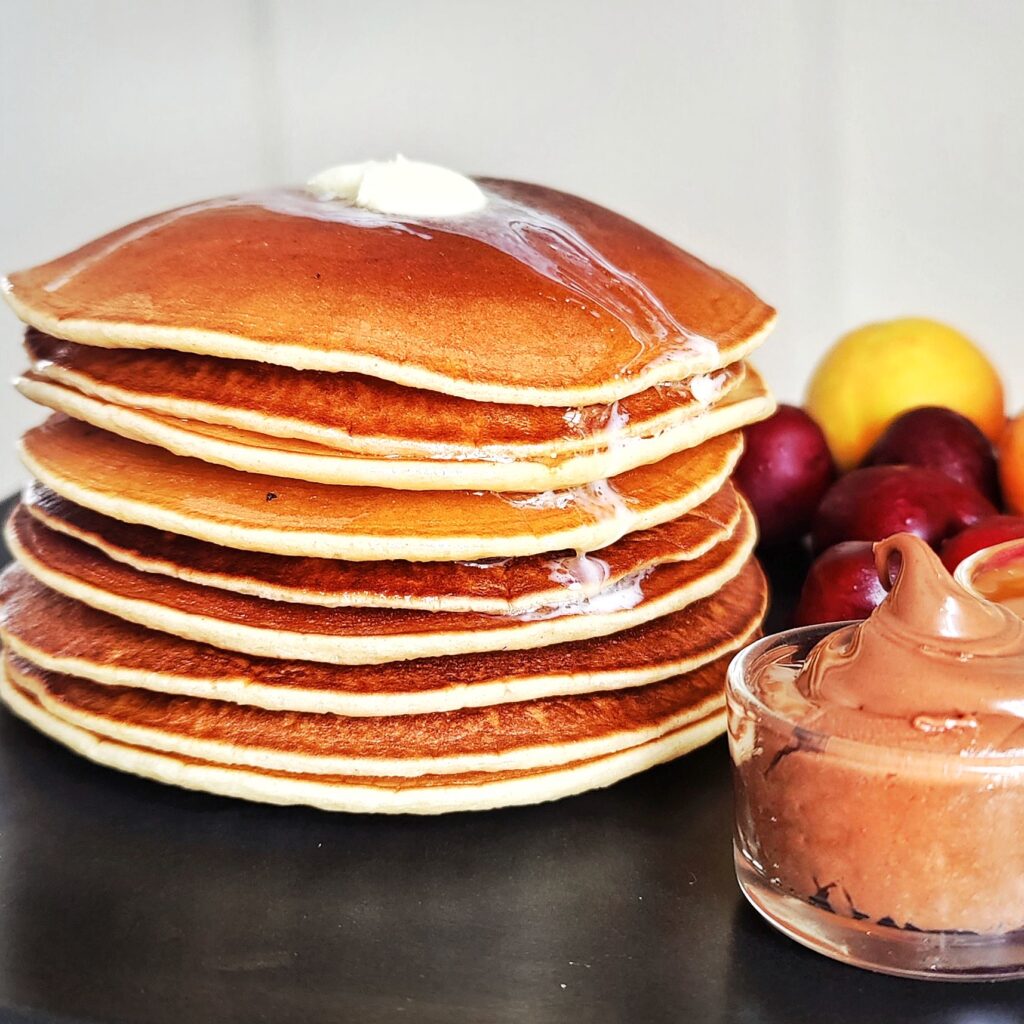 stack of pancakes with butter on top and fruit and chocolate on the side